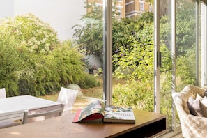Ein Zimmer mit Blick auf einen Garten durch große Fenster, ein Holztisch, ein Stuhl und ein Buch mit dem Titel 'Carefully Curated'.