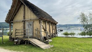 Une structure rustique en bois, dotée d’un toit de chaume, d’une porte en bois et d’une rampe menant à une plateforme.