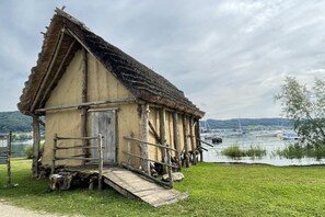 Eine rustikale Holzhütte mit einem strohgedeckten Dach, einer Holztür und einer Rampe, die zu einer Plattform führt.