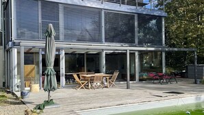 Une maison moderne dotée d’un patio entièrement vitré, de mobilier d’extérieur et d’une piscine.