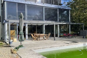 Ein modernes Haus mit einer gläsernen Terrasse, Gartenmöbeln und einem Swimmingpool.