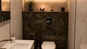 Un baño con pared de mármol, un lavabo blanco, inodoro y un pequeño cubo de basura.