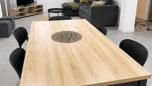 Una sala de estar moderna con una mesa de comedor de madera, sillas negras, un sofá gris y un televisor de pantalla plana.