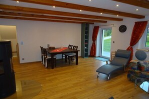 Um quarto espaçoso com piso de madeira, uma mesa de jantar com cadeiras, um sofá, uma poltrona reclinável e uma televisão.