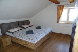 Quarto com estrutura de cama de madeira, janela com cortinas e radiador.