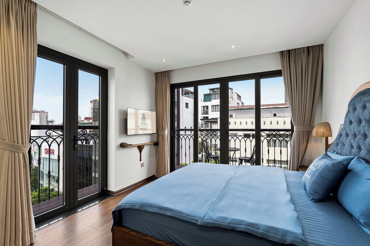 A hotel room with a large bed, a balcony with a view of the city, and a mounted TV on the wall.