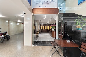 A hotel entrance with a reception desk, seating area, and a motorcycle parked outside. - House of Hanoi (Hai Ba Trung)