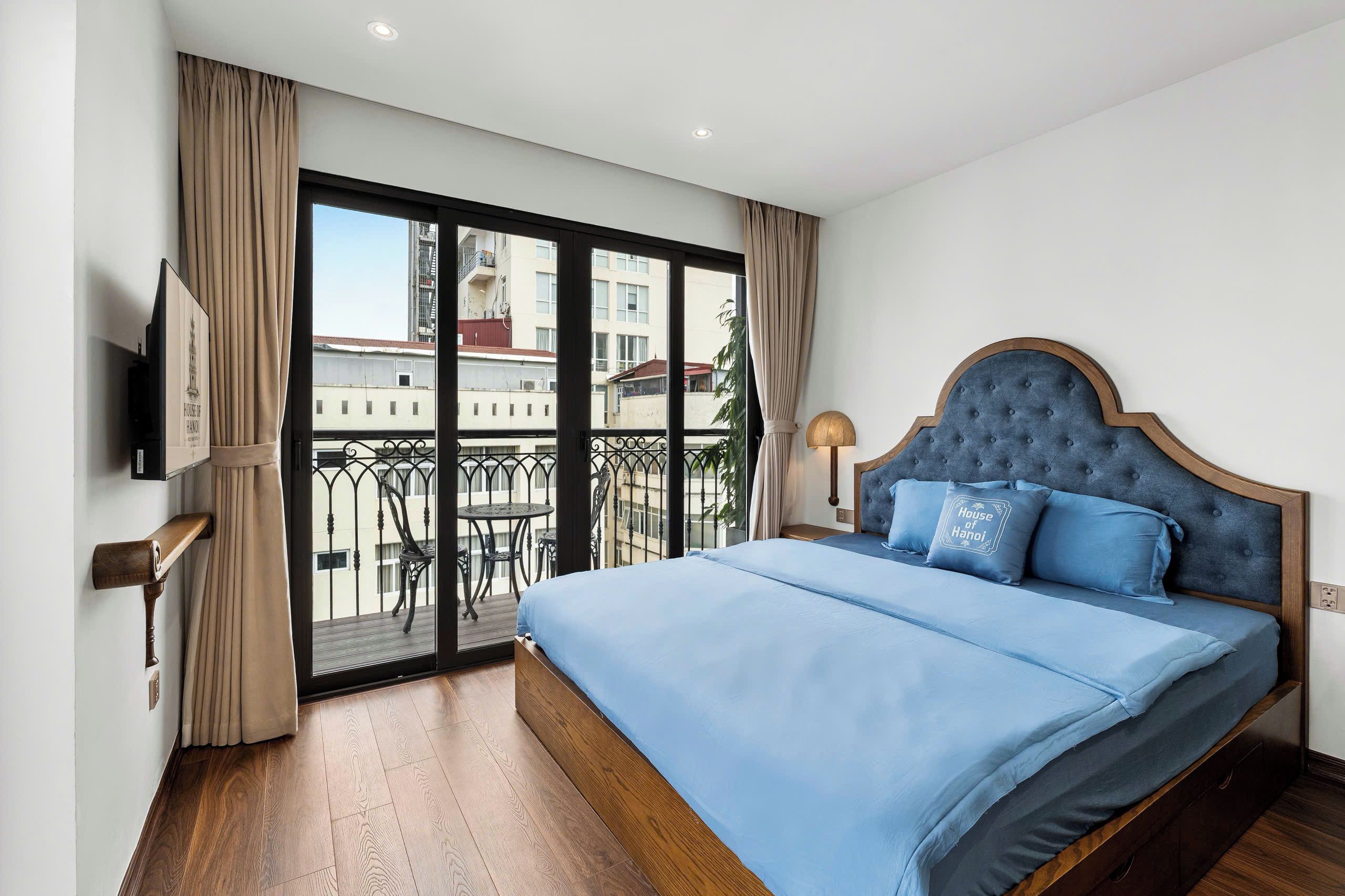 A hotel room with a large bed, a television on the wall, and a balcony with a view of the city.