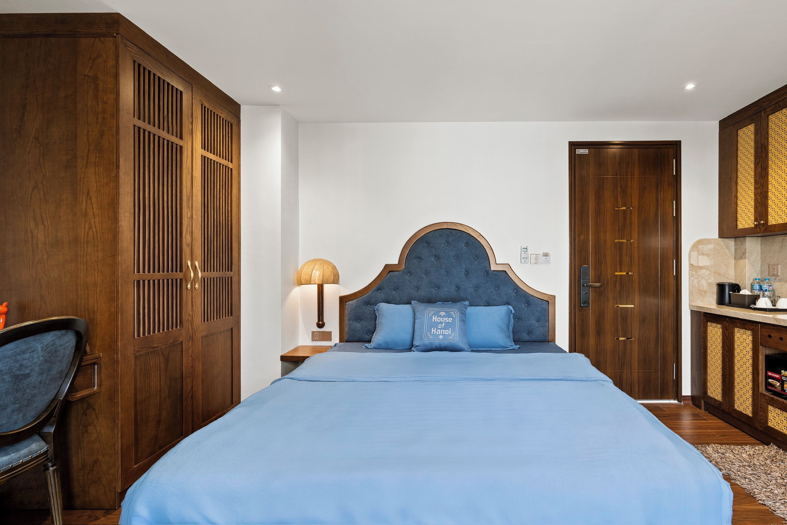 A hotel room with a large bed, wooden wardrobe, and a kitchenette area.