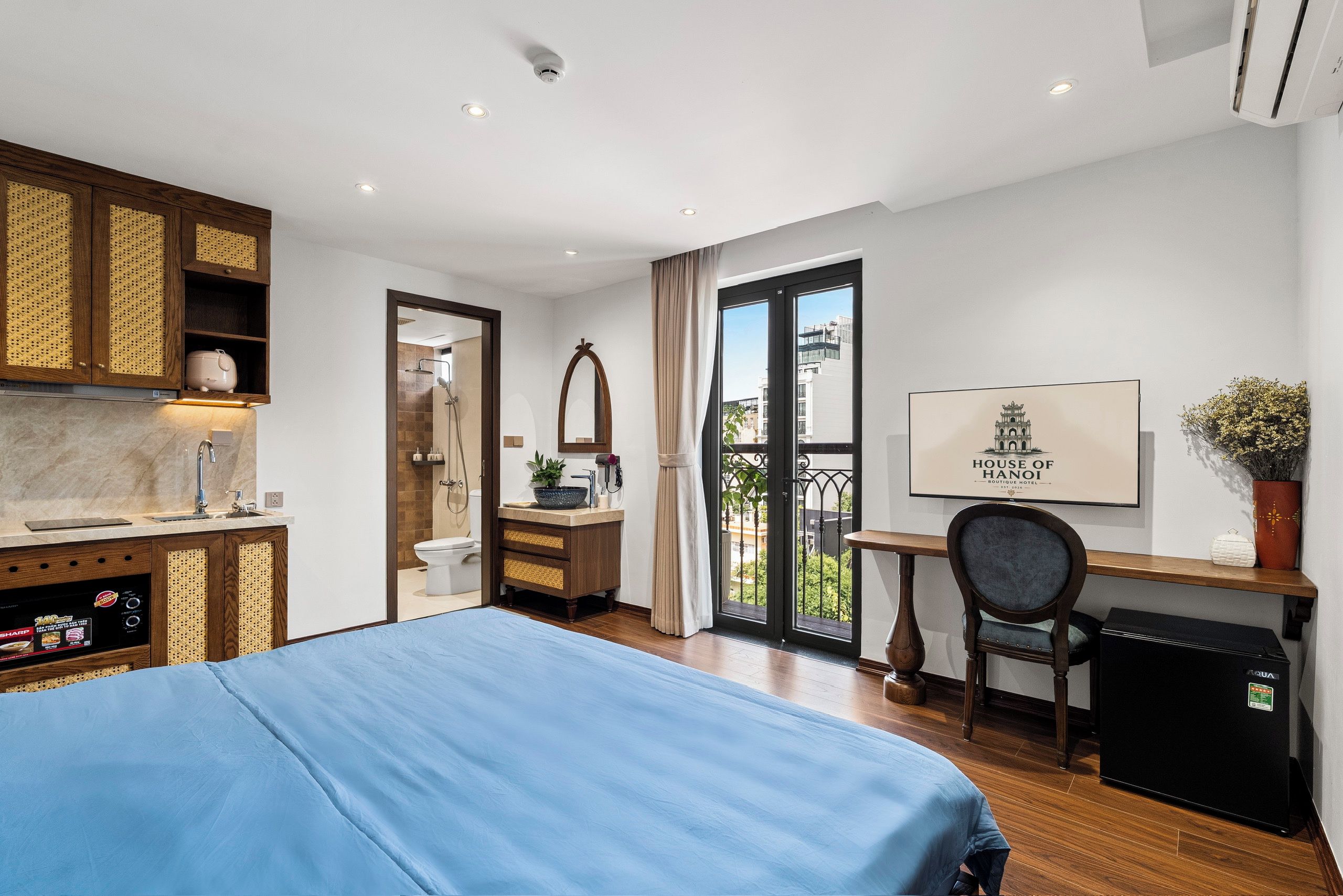 A hotel room with a bed, a desk, a chair, a minibar, a bathroom, and a view of the outside.