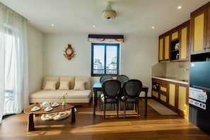 A living room with a sofa, a coffee table with teapots, a dining area with chairs, a window with a view, and a kitchen with a refrigerator. - House of Hanoi (Hai Ba Trung)