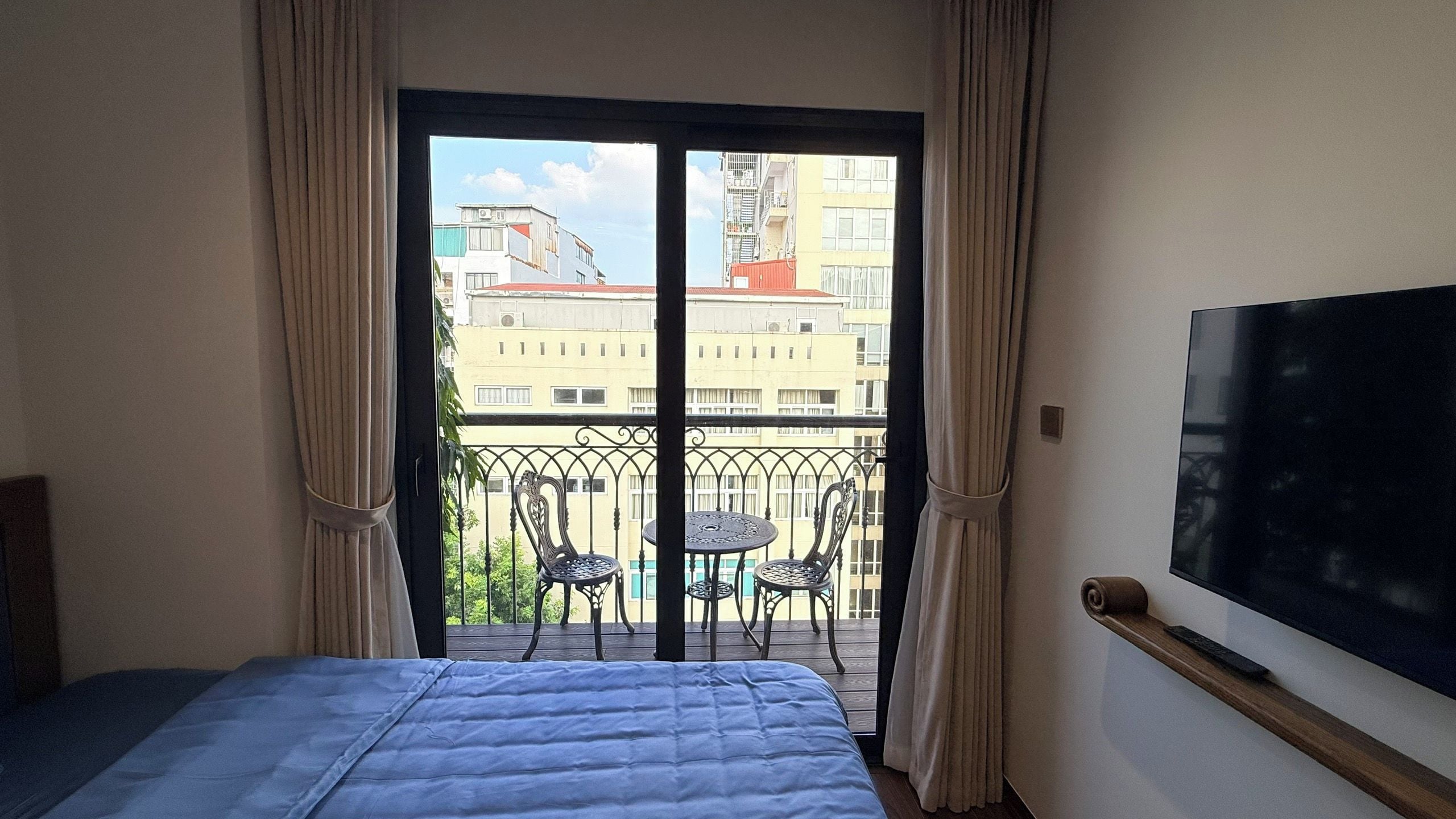 Ein Hotelzimmer mit Bett, einem an der Wand befestigten Fernseher und einem Balkon mit Tisch und Stühlen.