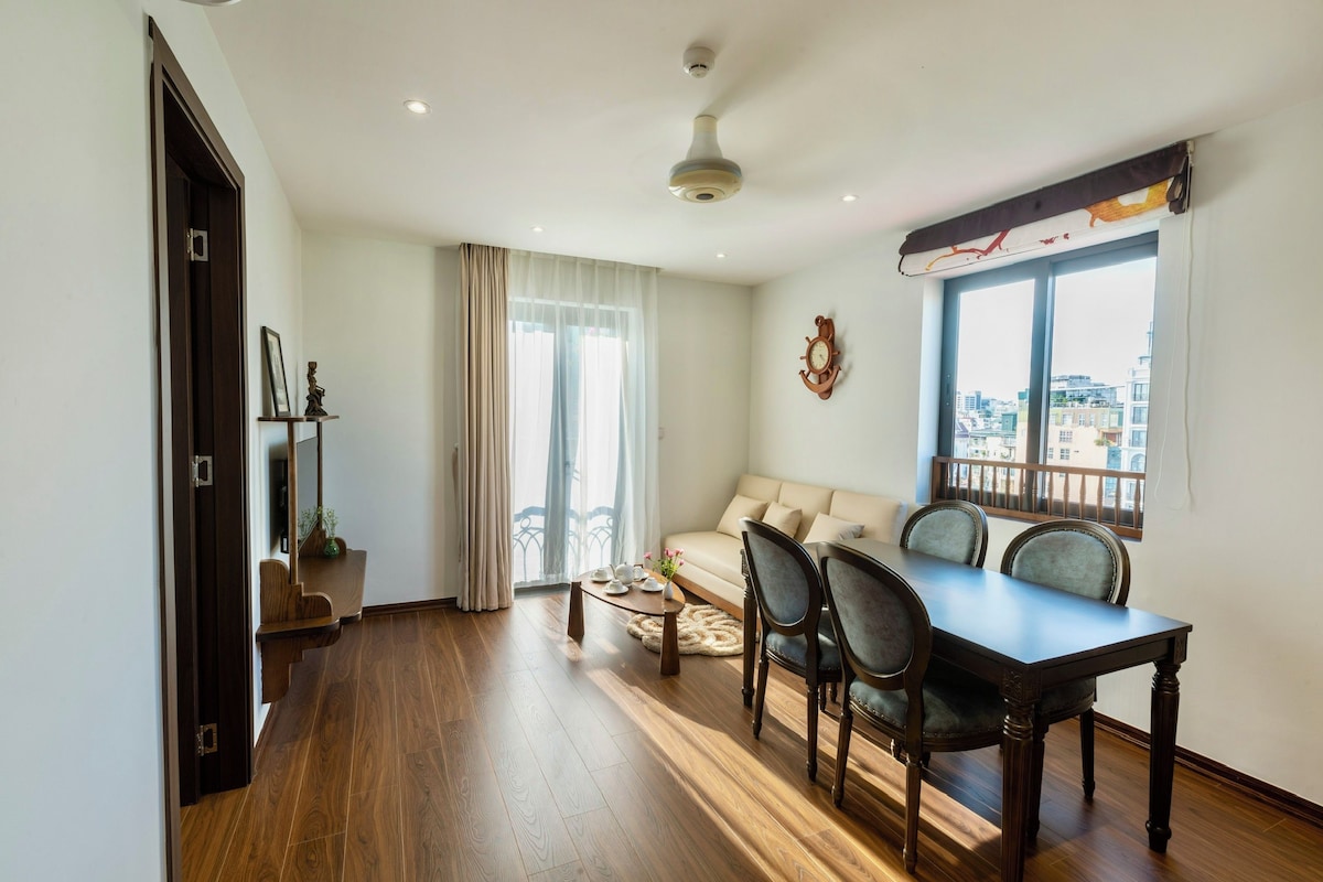 A living room with a sofa, dining table, chairs, and a view of the city through large windows.