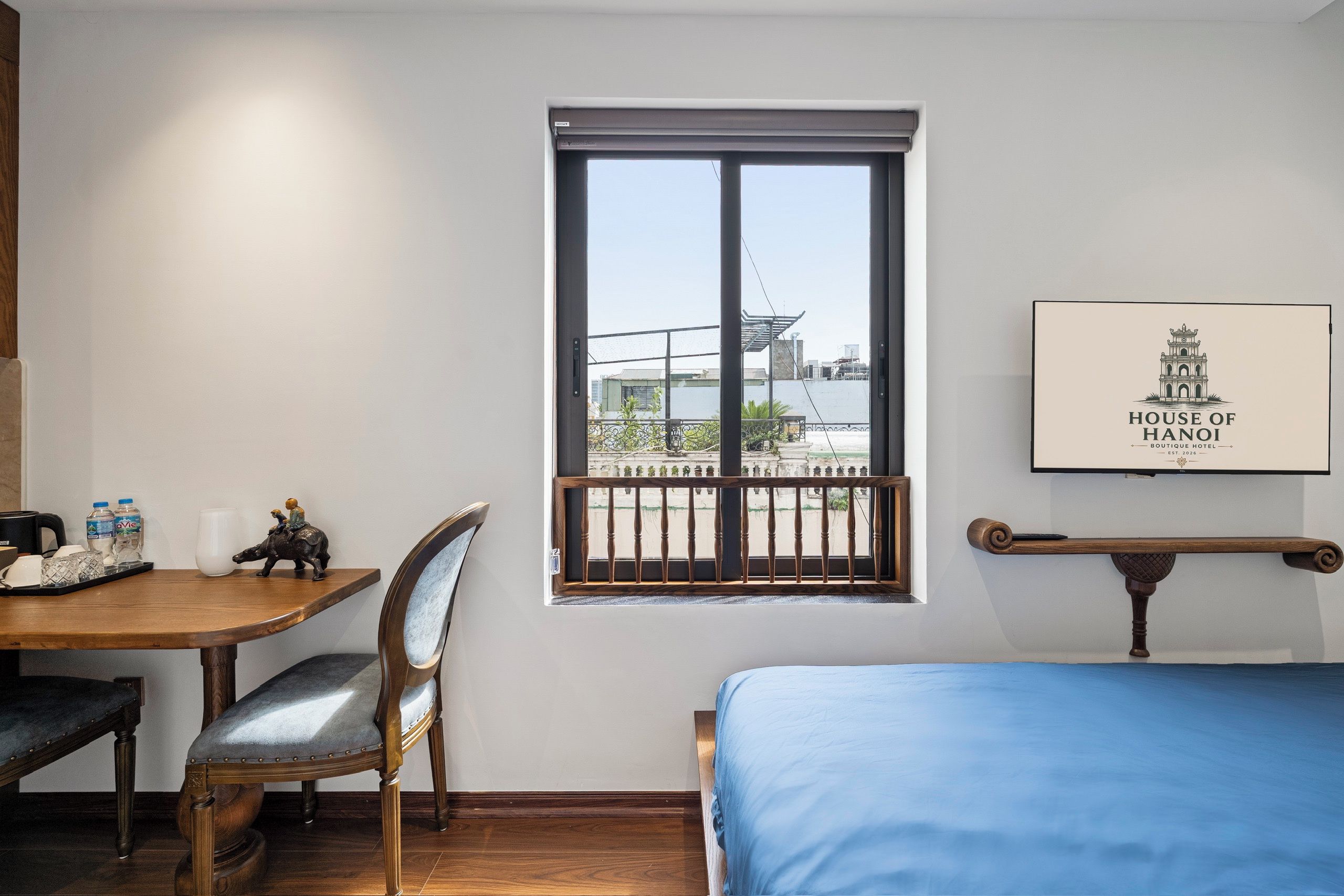Ein Hotelzimmer mit einem Bett, einem Schreibtisch mit Stuhl, einem Fenster mit Blick auf Gebäude und einem gerahmten Bild an der Wand.