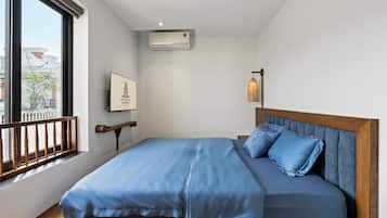Habitación de hotel con cama, ventana, equipo de aire acondicionado, un cuadro enmarcado y una lámpara colgante.