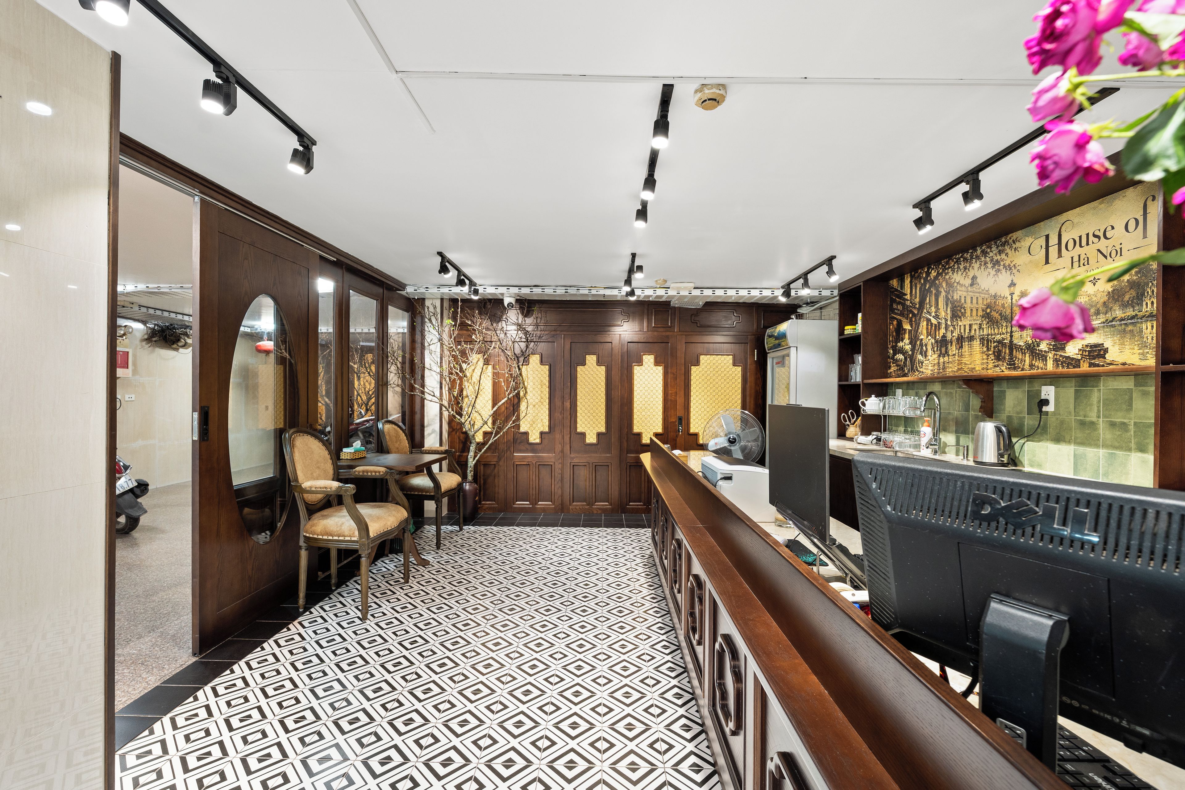 A hotel lobby with a patterned floor, wooden furniture, a reception desk, and a wall with a decorative panel.