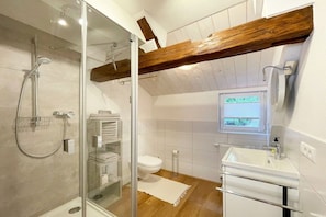 Casa de banho moderna com cabine de duche em vidro, viga de teto em madeira, lavatório branco e sanita.