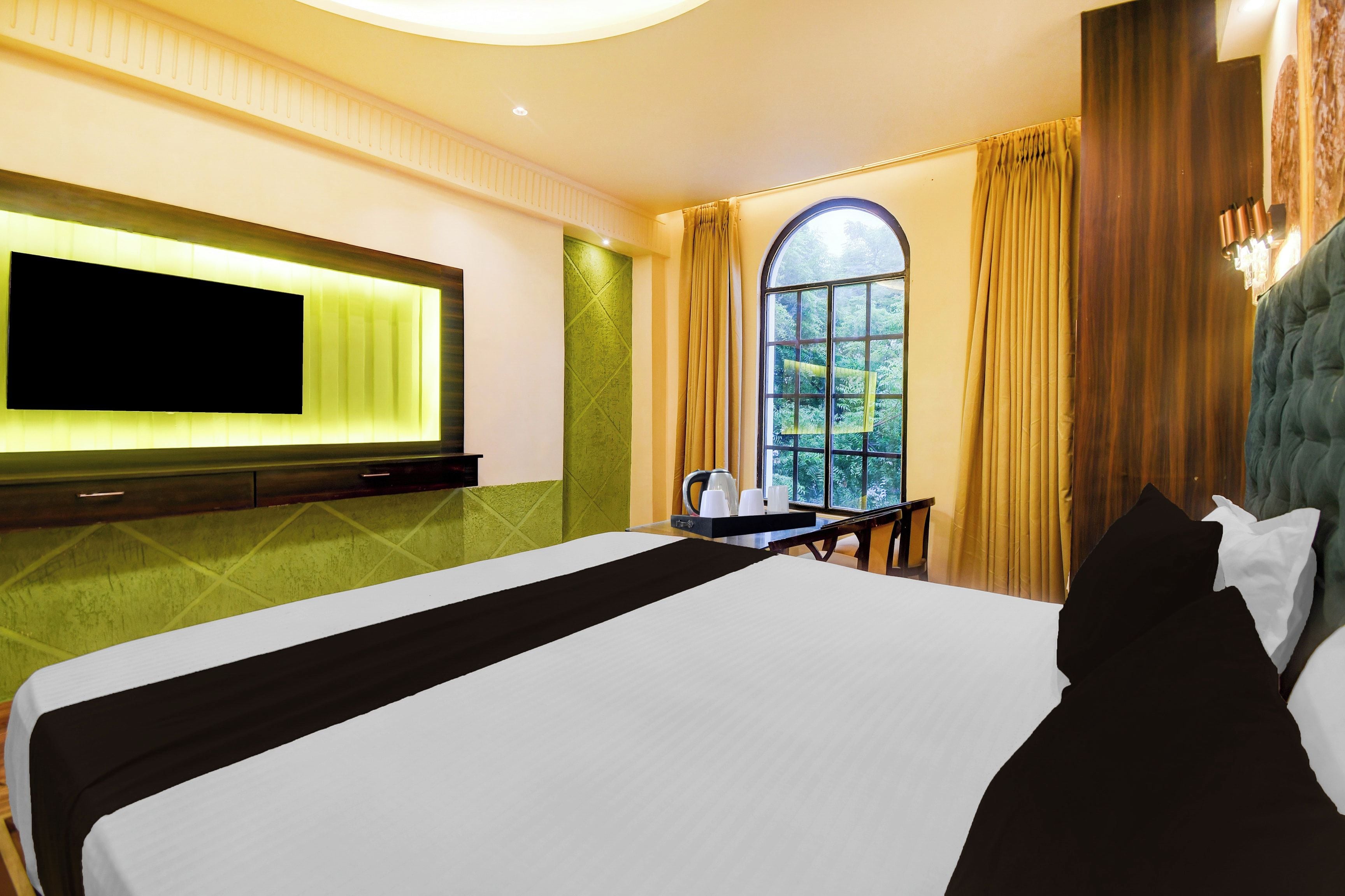 Une chambre d’hôtel avec un grand lit, un téléviseur à écran plat fixé au mur, une fenêtre avec des rideaux et une vue sur la verdure environnante.