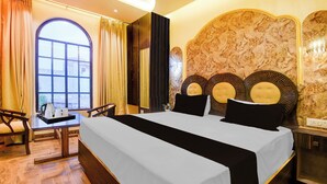 A hotel room with a large bed, a desk with a chair, a view through a window, and a decorative headboard. - Super OYO Townhouse Varanasi Railway (Varanasi)
