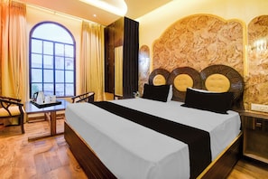 Ein Hotelzimmer mit einem großen Bett, einem Schreibtisch mit Stuhl, Blick durch ein Fenster und einem dekorativen Kopfteil.