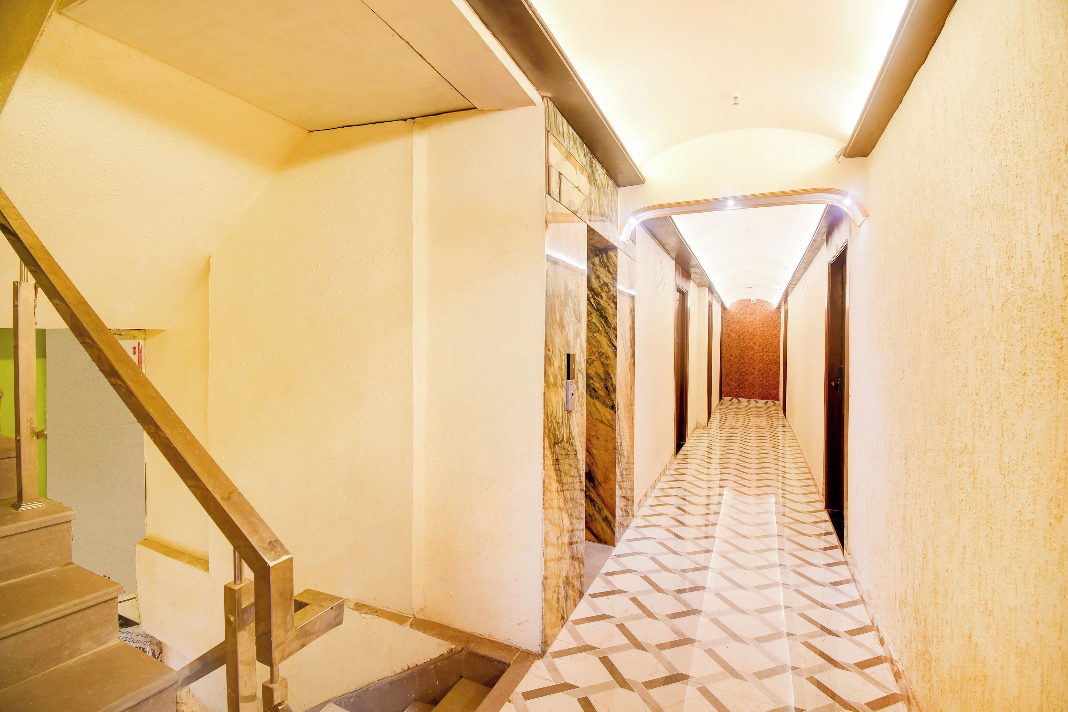 Un pasillo de hotel con piso estampado, una escalera a la izquierda y una puerta al final.