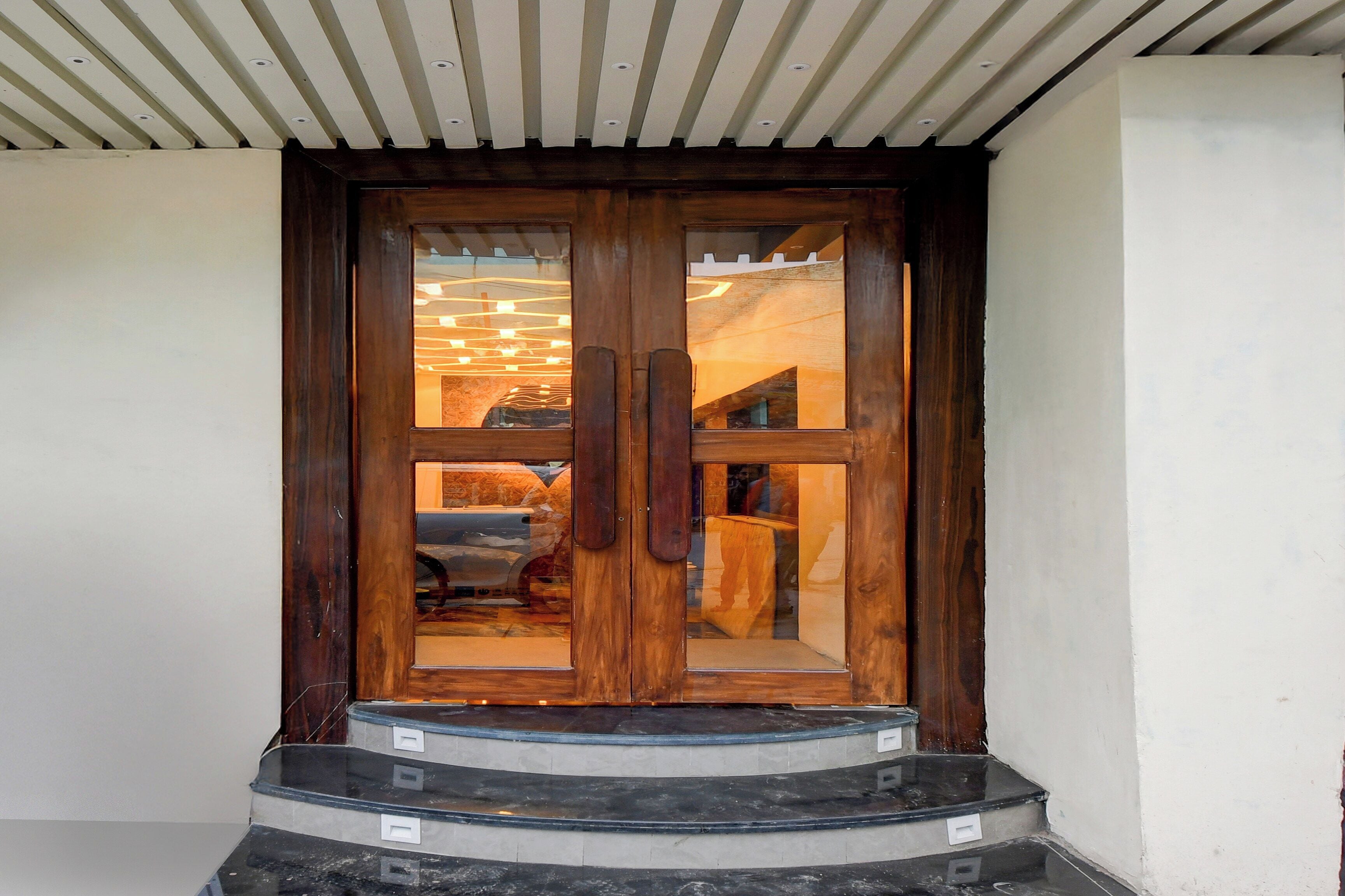 Puerta doble de madera con paneles de vidrio, que da a una escalera con piso de baldosas negras y grises.