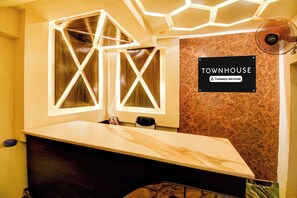 Zona de recepción de un hotel con mostrador de mármol, un cartel que indica que es una casa señorial de servicio empresarial y un diseño geométrico único en el techo.