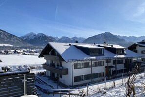 Hotel moderno com telhado plano, janelas amplas e vista para montanhas cobertas de neve.