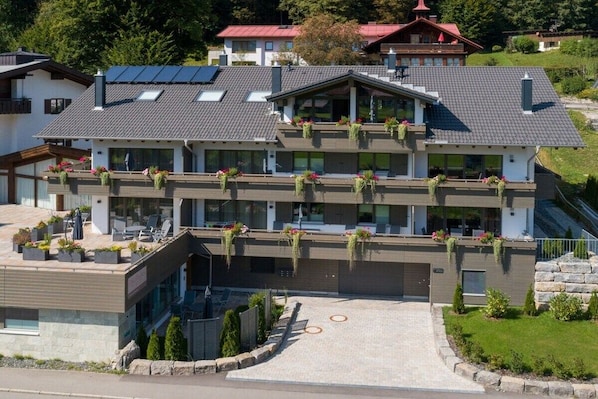Um edifício de vários andares com varandas, entrada com calçada e jardim ajardinado.