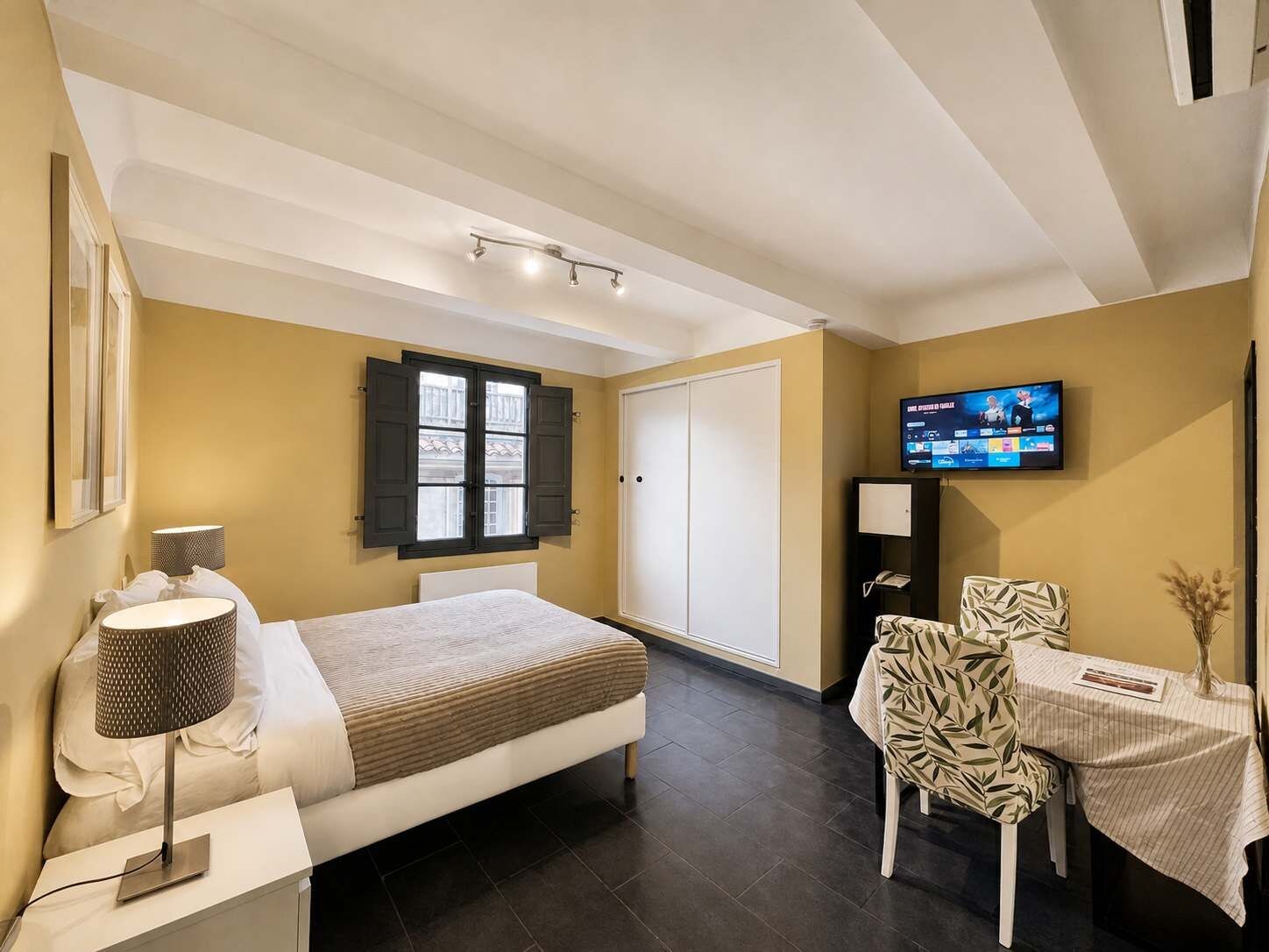 Une chambre d’hôtel avec un lit, une table de chevet, une lampe, une télévision et une petite table avec une chaise.