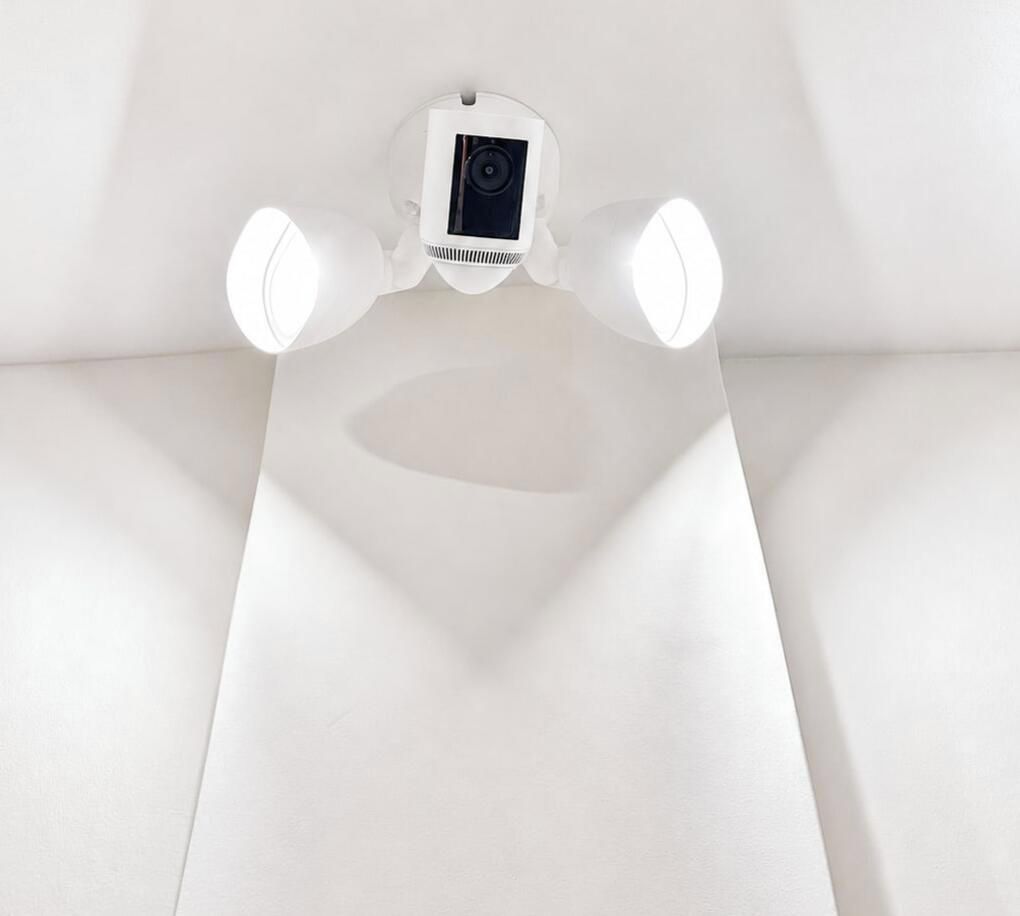 Une caméra de surveillance fixée au plafond, dotée d’un boîtier blanc et d’un objectif visible.