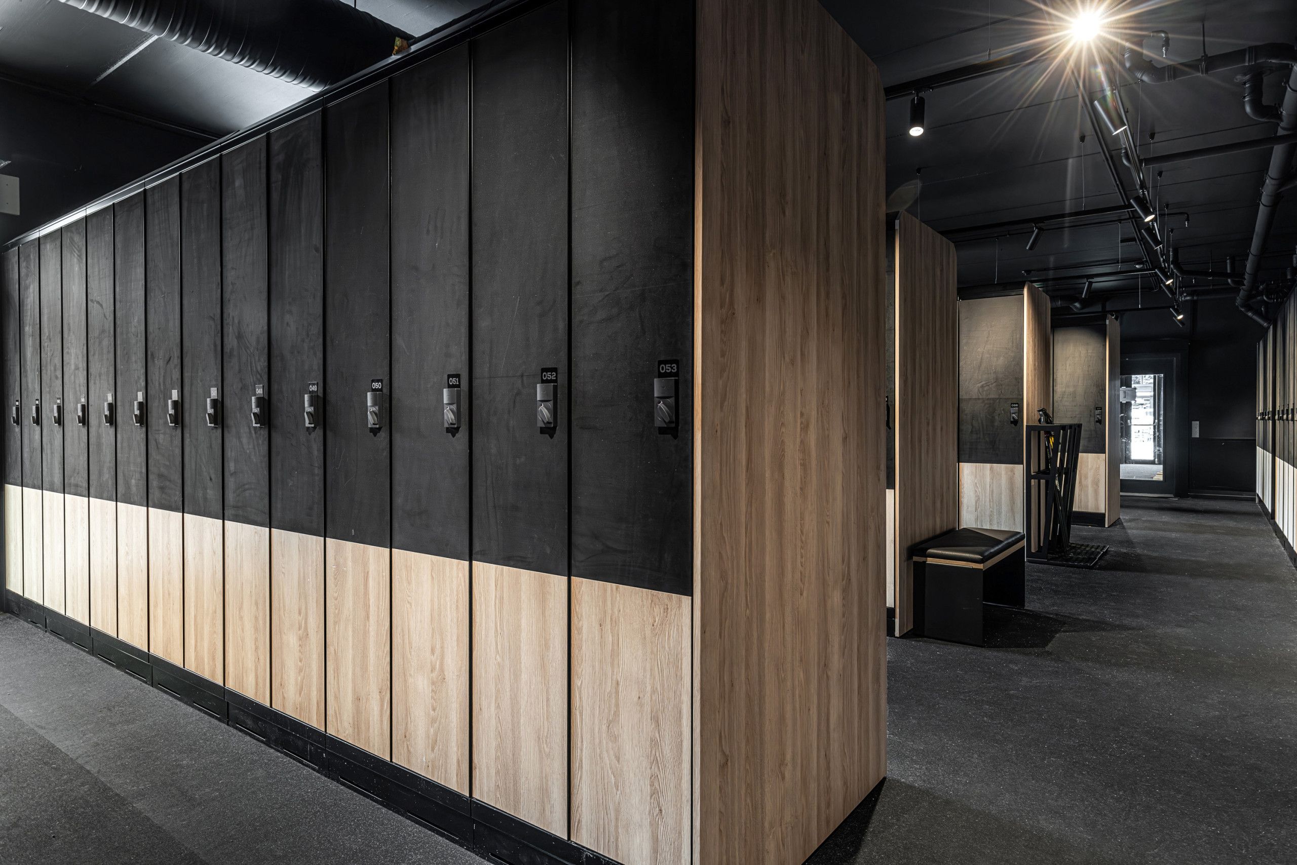A row of lockers with numbers, a bench, and a trash bin in a hallway.