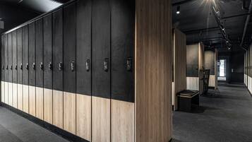 A row of lockers with numbers, a bench, and a trash bin in a hallway.