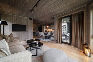 A modern living room with a sofa, a coffee table, and a TV mounted on the wall. - Exclusive Slopeside Living in Hemsedal (Hemsedal)