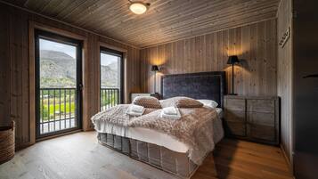 A bedroom with a large bed, wooden walls, a view through a window, and a ceiling light.