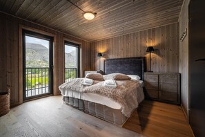 A bedroom with a large bed, wooden walls, a view through a window, and a ceiling light. - Exclusive Slopeside Living in Hemsedal (Hemsedal)