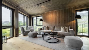 Amplia habitación con piso de madera, un sofá, sillones, una mesa de centro y ventanas amplias que ofrecen vistas al exterior.