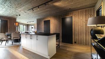 A modern kitchen with a central island, wooden walls, and a dining area with chairs and a table.