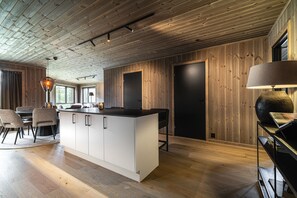 A modern kitchen with a central island, wooden walls, and a dining area with chairs and a table. - Exclusive Slopeside Living in Hemsedal (Hemsedal)