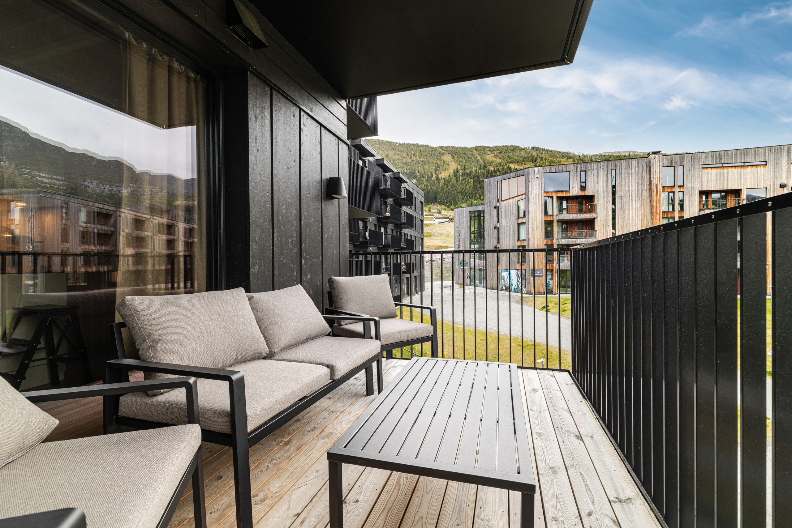 Een balkon met een bank en stoelen, met uitzicht op een woongebied met moderne gebouwen.