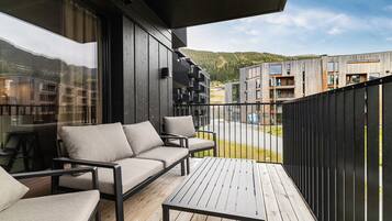 Een balkon met een bank en stoelen, met uitzicht op een woongebied met moderne gebouwen.