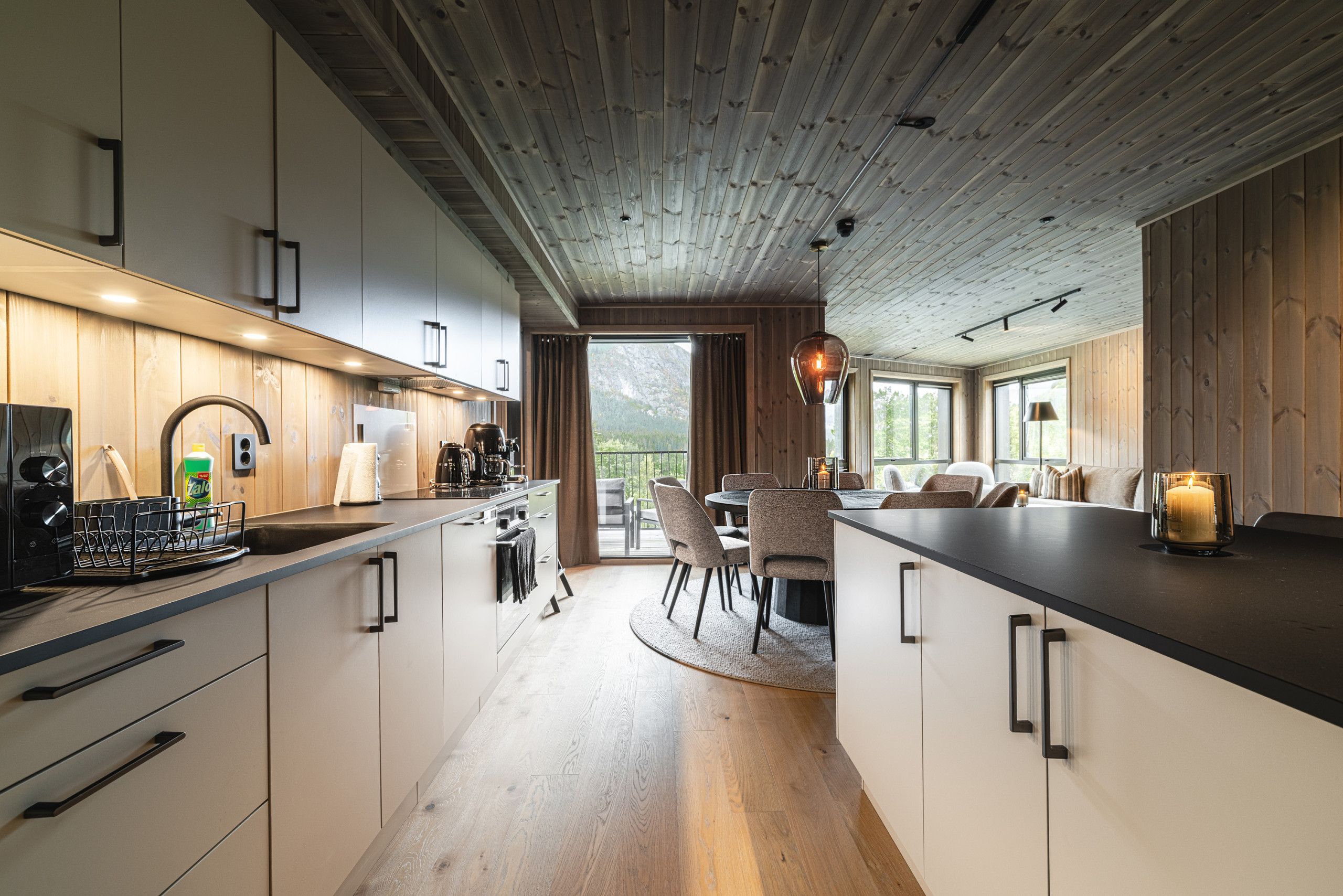 Una cocina moderna con armarios de madera, un comedor con mesa y sillas redondas, y vistas al exterior a través de amplios ventanales.