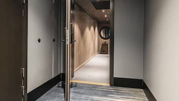 A hotel hallway with a carpeted floor, a door on the left, and a circular window on the right.
