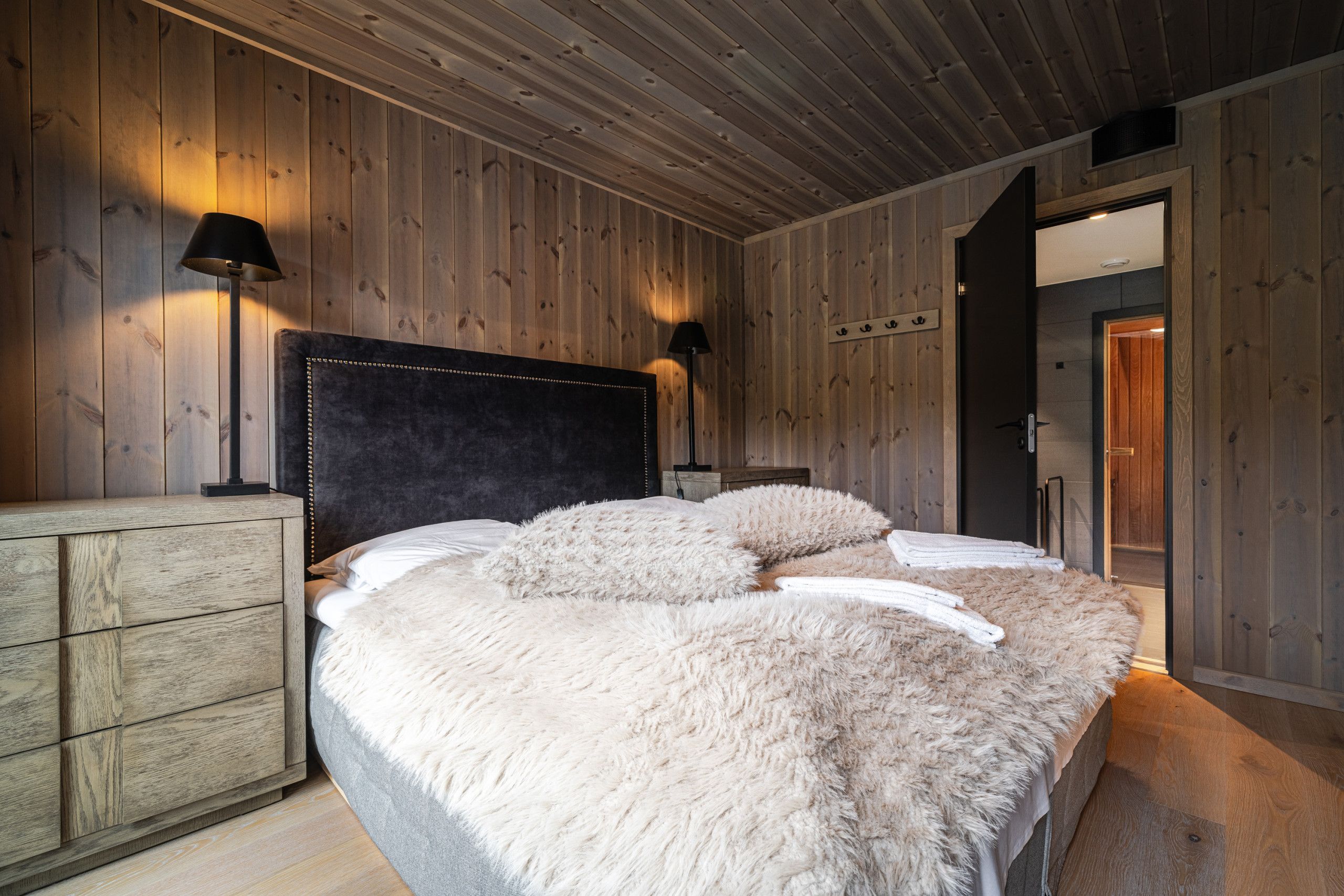 Un dormitorio con una cama grande, paredes de madera, cabecera, lámparas de noche y un aparador de madera.