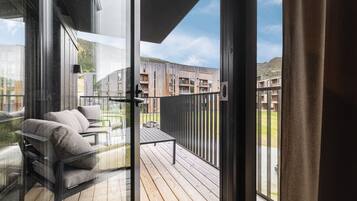 A balcony with a sofa and a table, overlooking a modern building and a mountainous landscape.