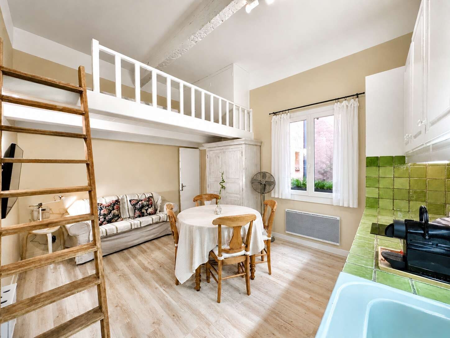Un espace de vie compact comprenant une chambre en mezzanine, un coin repas et une kitchenette.