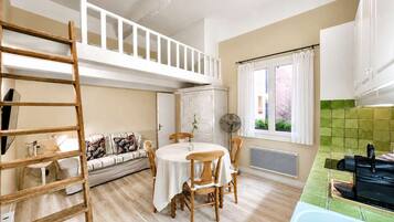 Un espace de vie compact comprenant une chambre en mezzanine, un coin repas et une kitchenette.