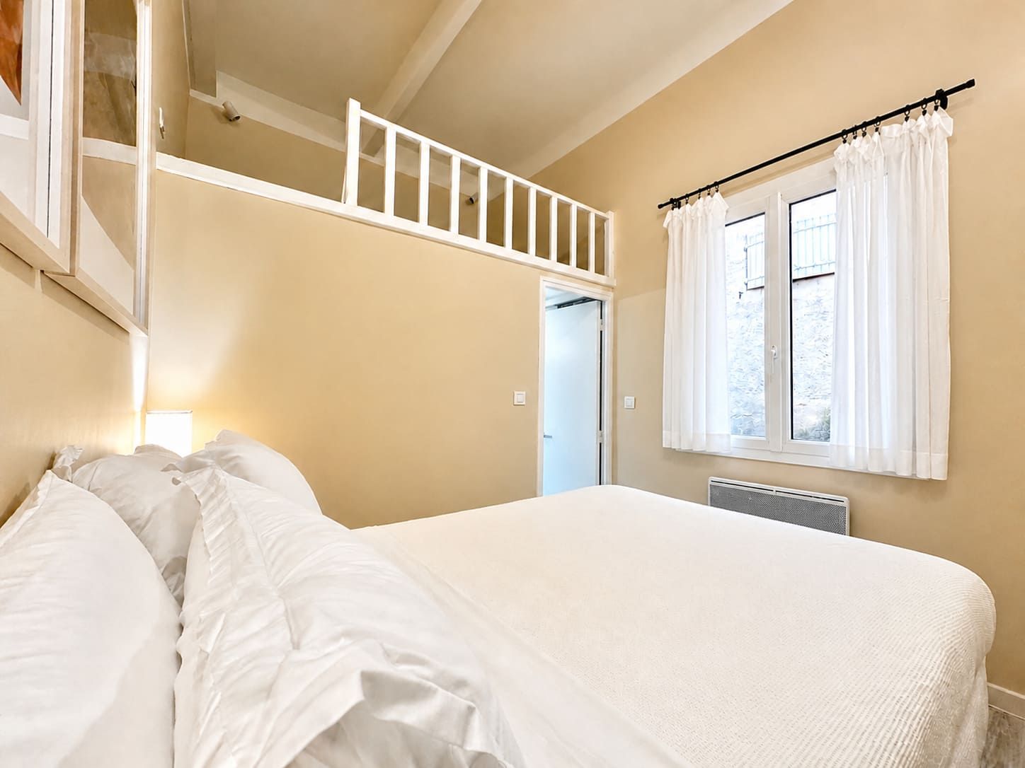 Una camera da letto con un letto, una finestra con tende, un termosifone e una porta che dà su un'altra stanza.