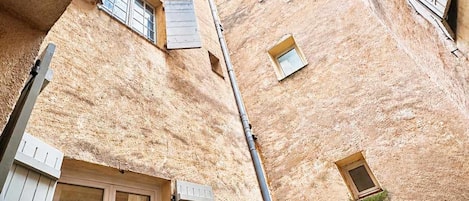 A narrow alleyway between buildings with wooden shutters and a clear blue sky above.