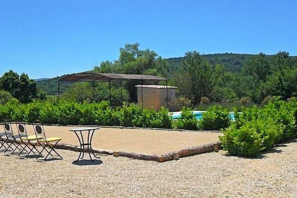 An outdoor seating area with a table and chairs, surrounded by a gravel path and greenery.